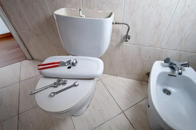 Toilet and sink in a small bathroom with tools resting on the toilet seat