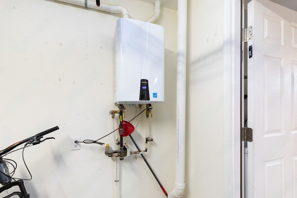 Wall-mounted water heater with pipes and a pressure valve in a utility room beside a door