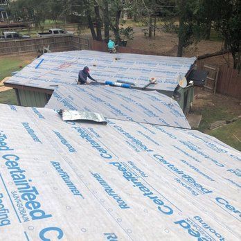 Roofers installing roofing material.  Workers on a roof, applying CertainTeed underlayment on an overcast day.