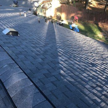 Dark gray shingle roof, with a long shadow cast, and people working nearby.