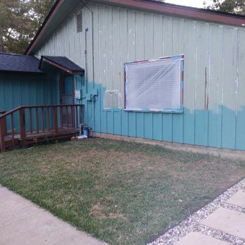 House exterior with turquoise siding being painted, window covered in plastic, small yard.