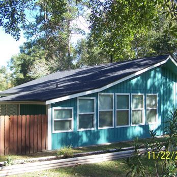 Blue house with white-framed windows, dark roof, wooden fence, and trees.
