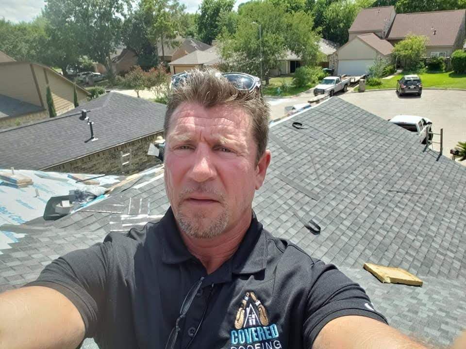 Man in blue shirt shakes hands with worker in uniform in front of a house.