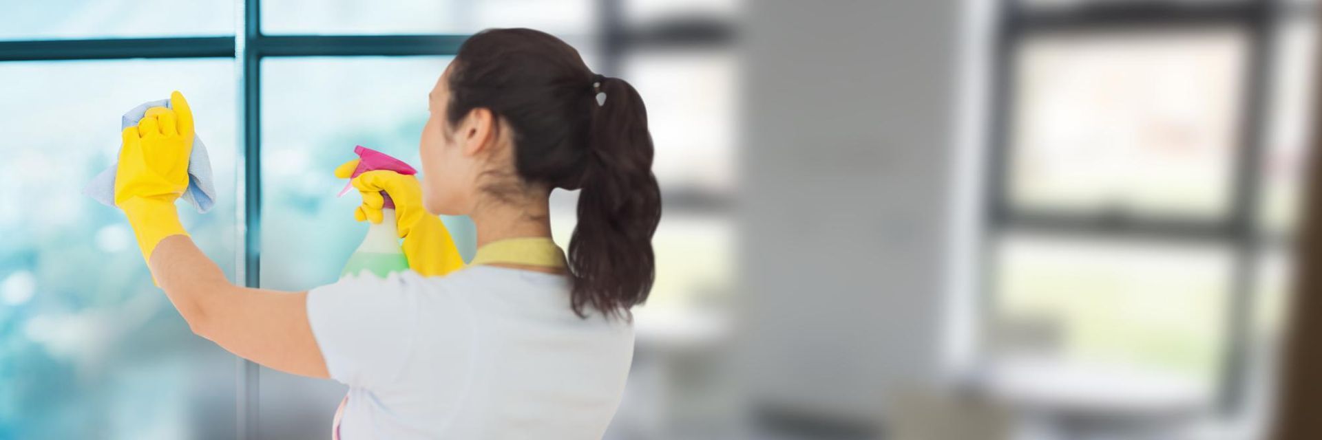 A woman in yellow gloves is cleaning a window with a cloth.