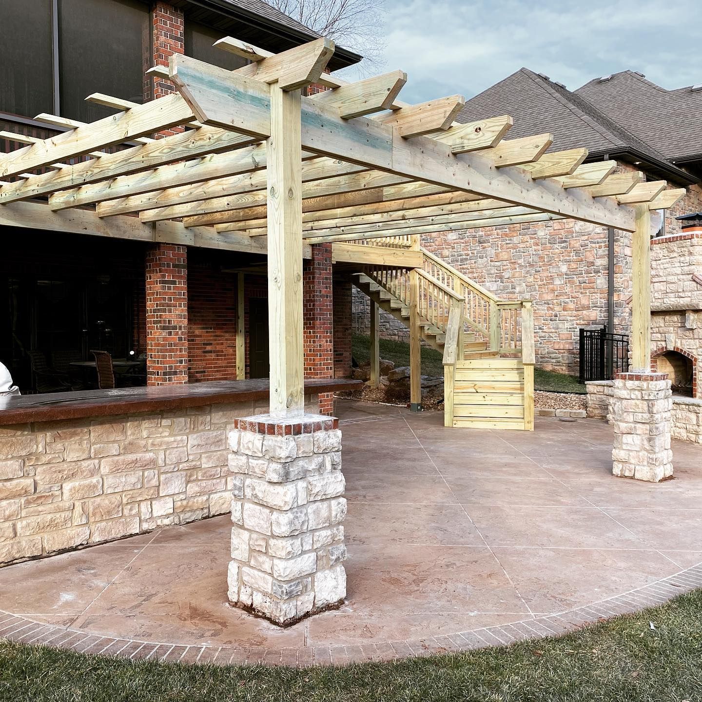 A wooden pergola is sitting on top of a patio next to a brick building.