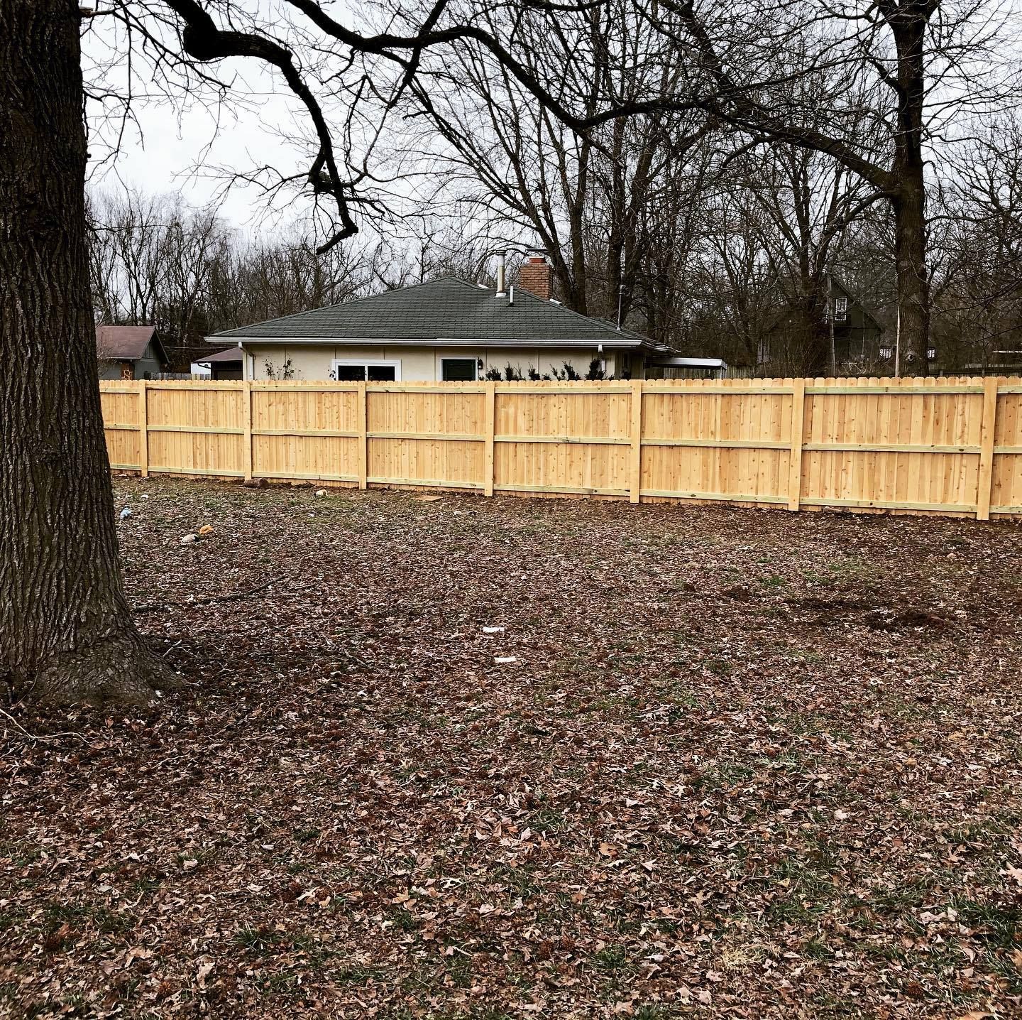 A wooden fence is in the backyard of a house surrounded by trees.