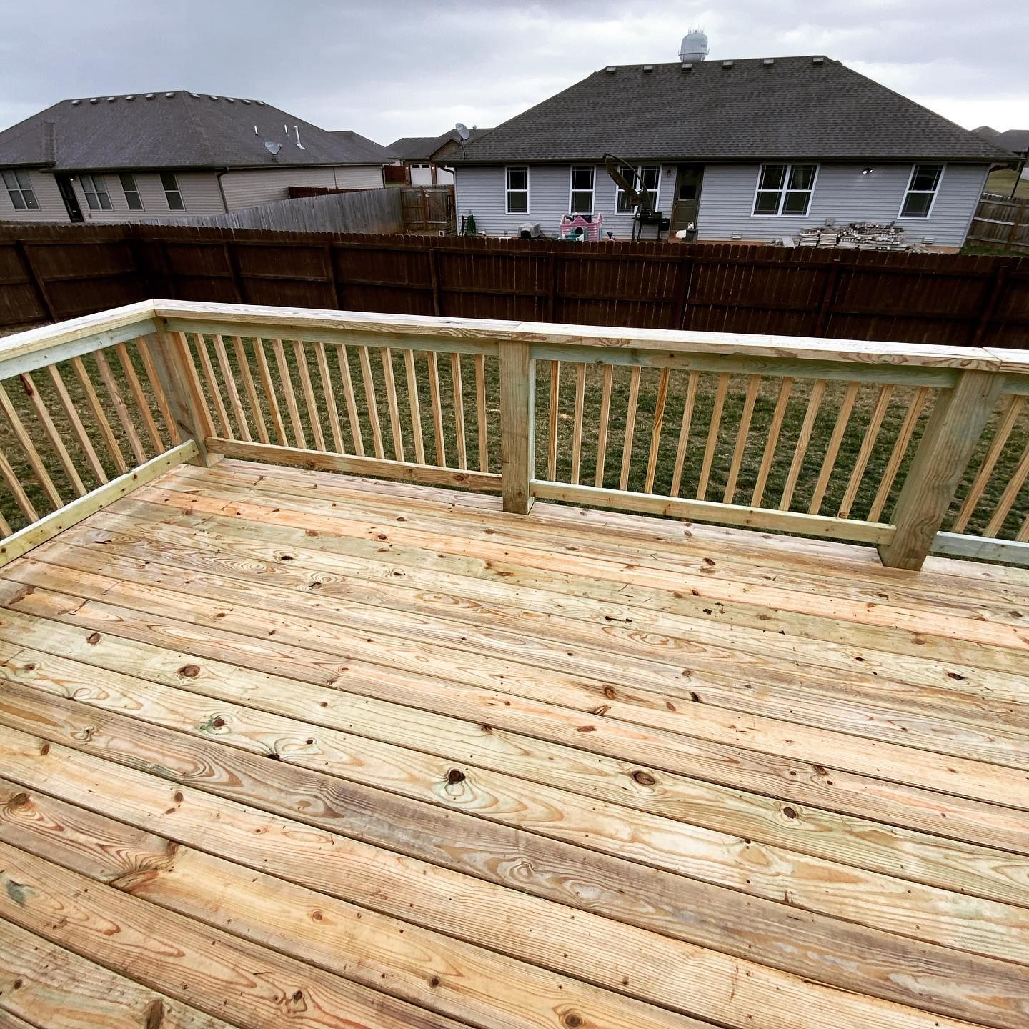 A wooden deck with a railing and a house in the background.