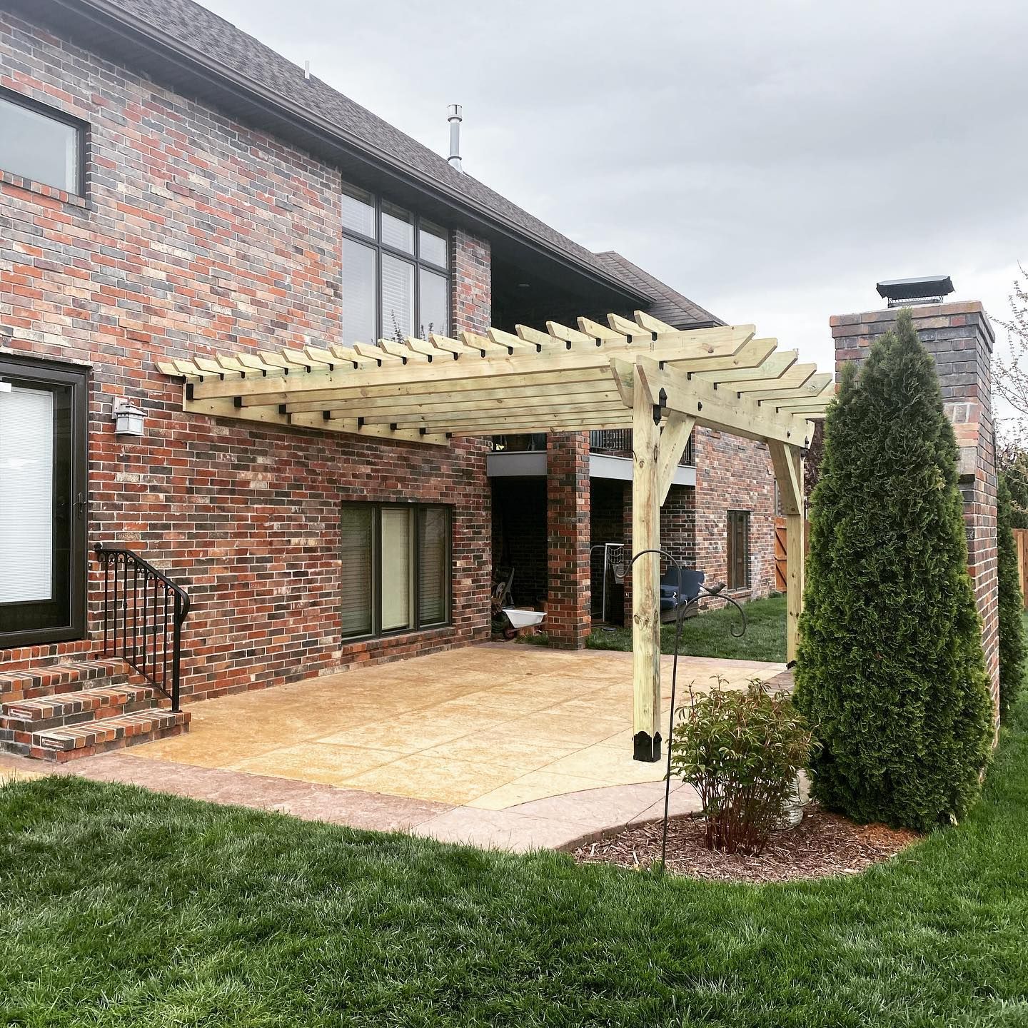 A wooden pergola is sitting in front of a brick house.