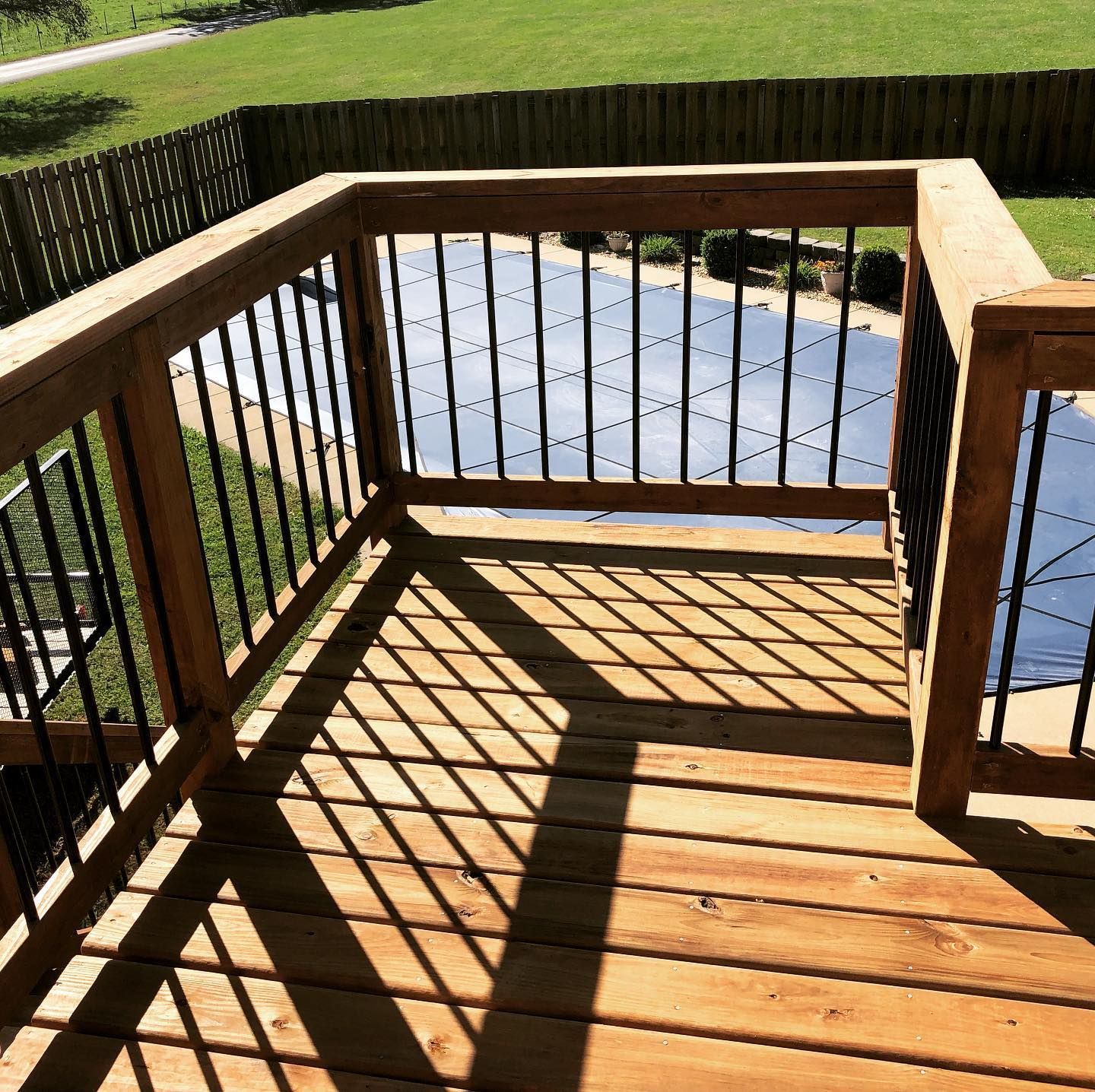 A wooden deck with a metal railing and a pool in the background