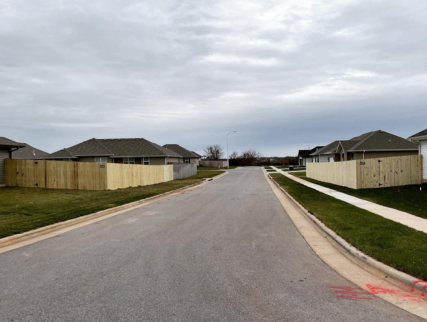 A wooden fence along the side of a road in a residential neighborhood.