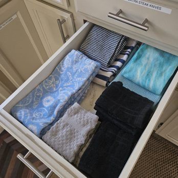Drawer holding various folded kitchen towels in shades of blue, black, and gray.