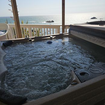 Hot tub with bubbly water overlooking the ocean on a sunny day, with a partial view of a deck.