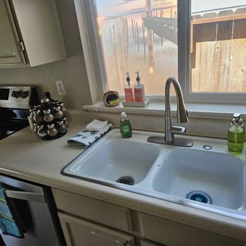 Kitchen sink with white countertop, window above, spices, and soap.