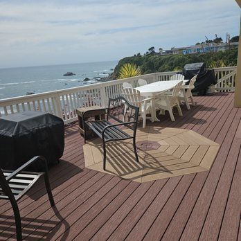 Wooden deck overlooking the ocean with a table, chairs, and grill.