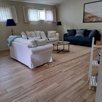 Living room with white couches, blue sofa, wooden floor, and large windows.