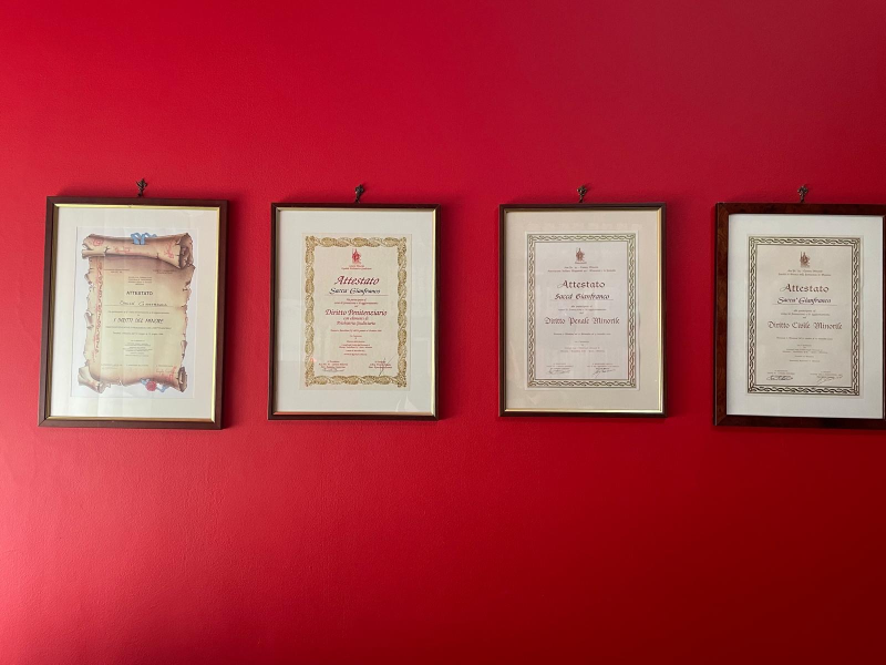 Quattro certificati incorniciati sono appesi su una parete rossa.