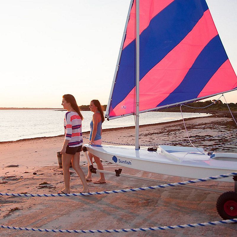 Two women walking on a beach next to a sailboat that says turbo