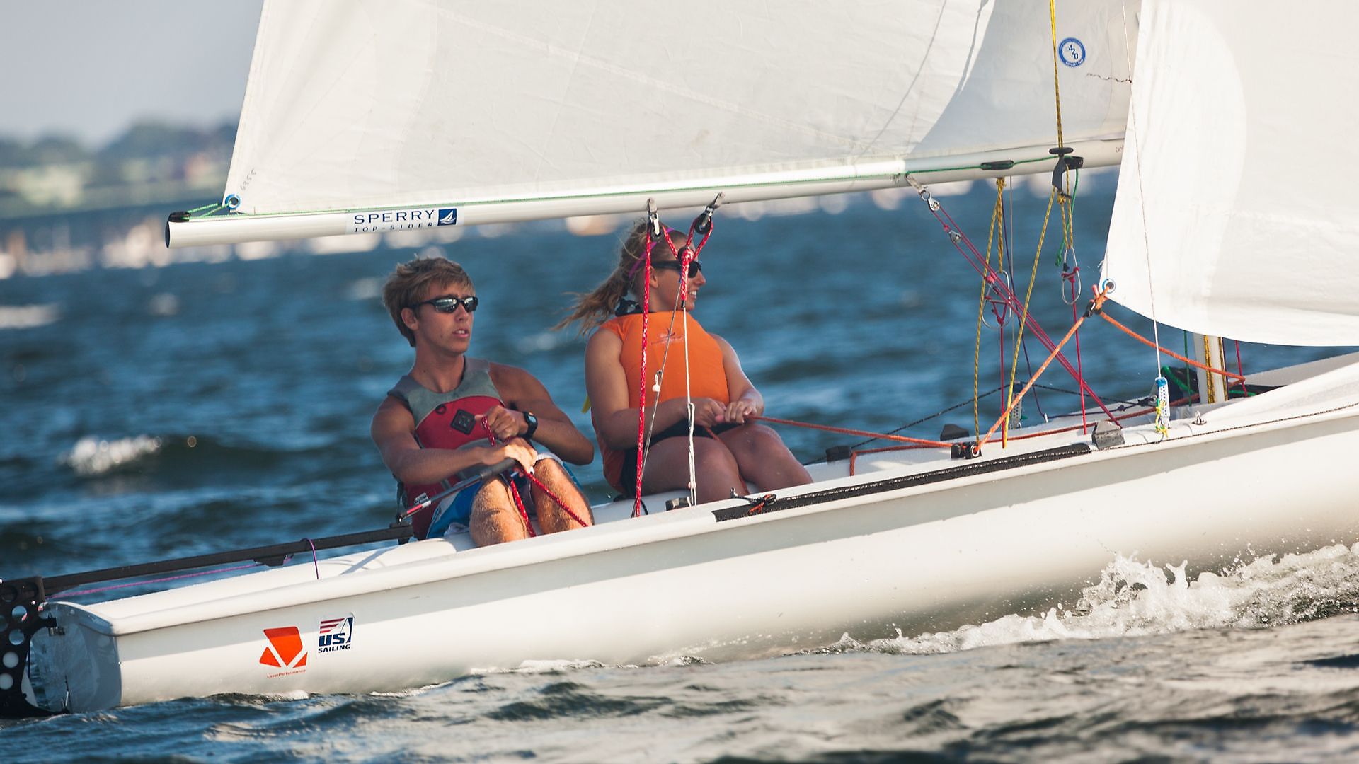 Two women are sitting on a sailboat in the ocean.