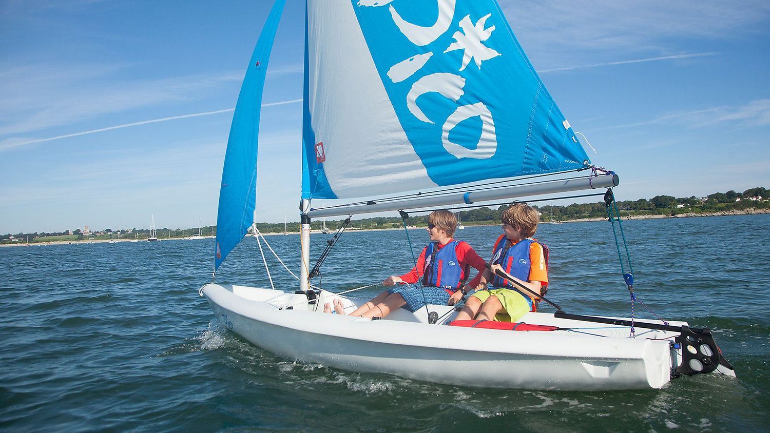 Two young boys are sailing a small sailboat on a lake.