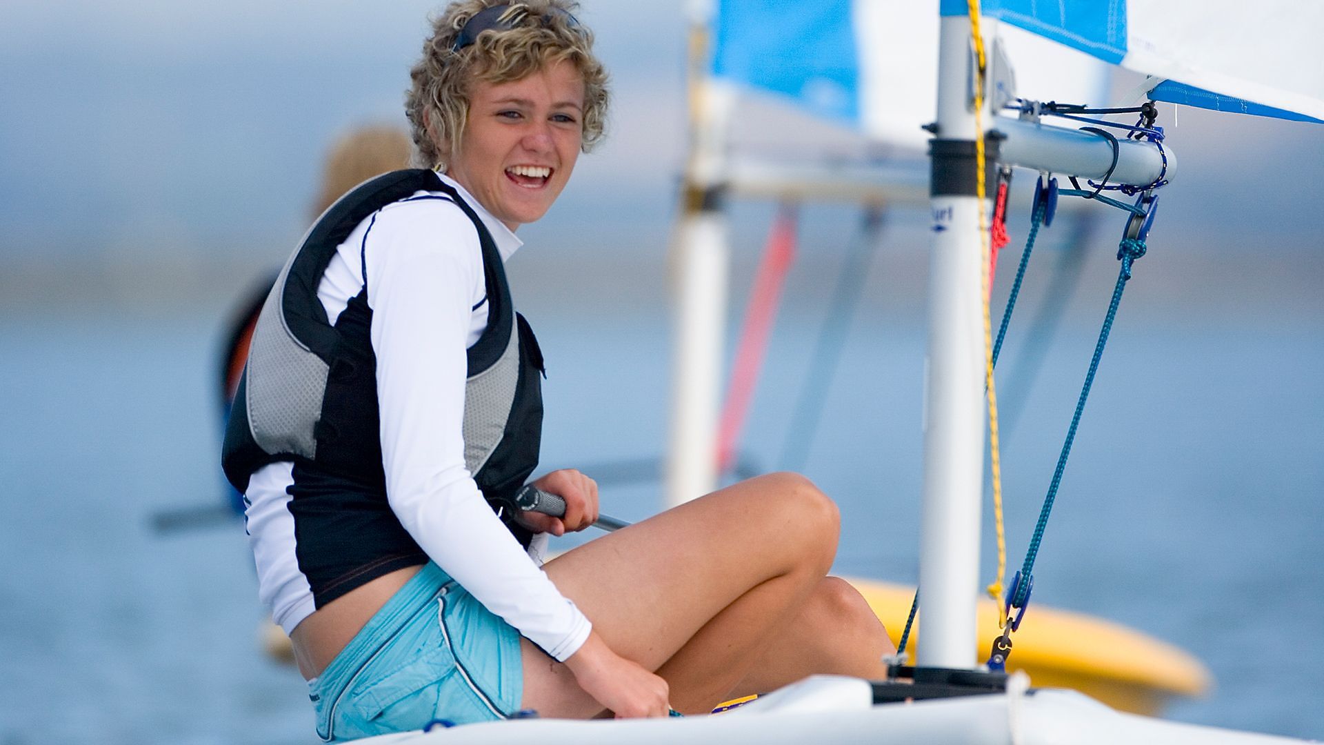 A woman is sitting on a sailboat in the water and smiling