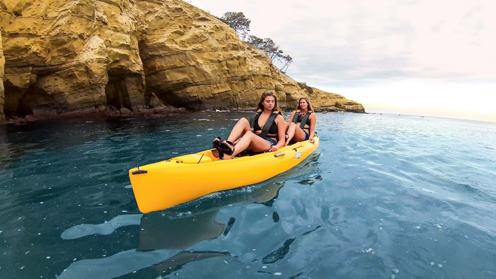 Two women are sitting in a yellow kayak in the ocean.