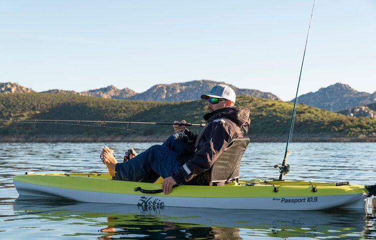 A man is sitting in a yellow kayak on a lake with a fishing rod.