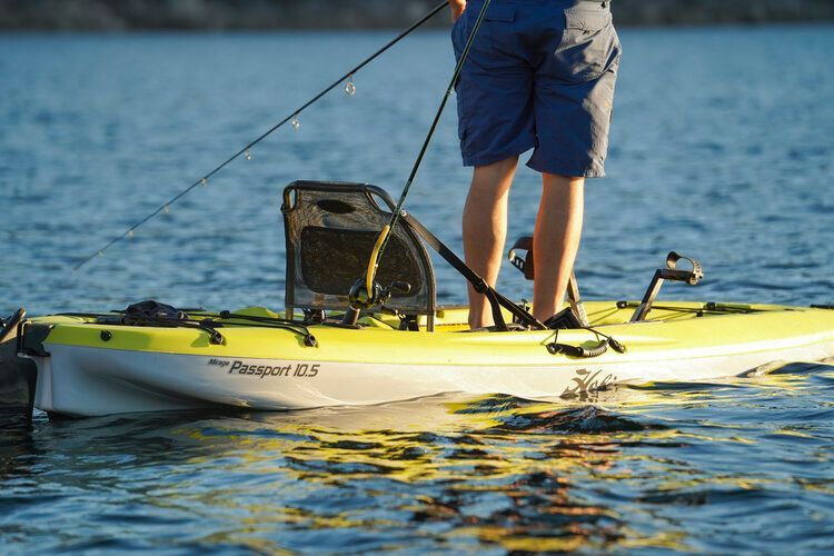 A man is standing on a kayak in the water holding a fishing rod.