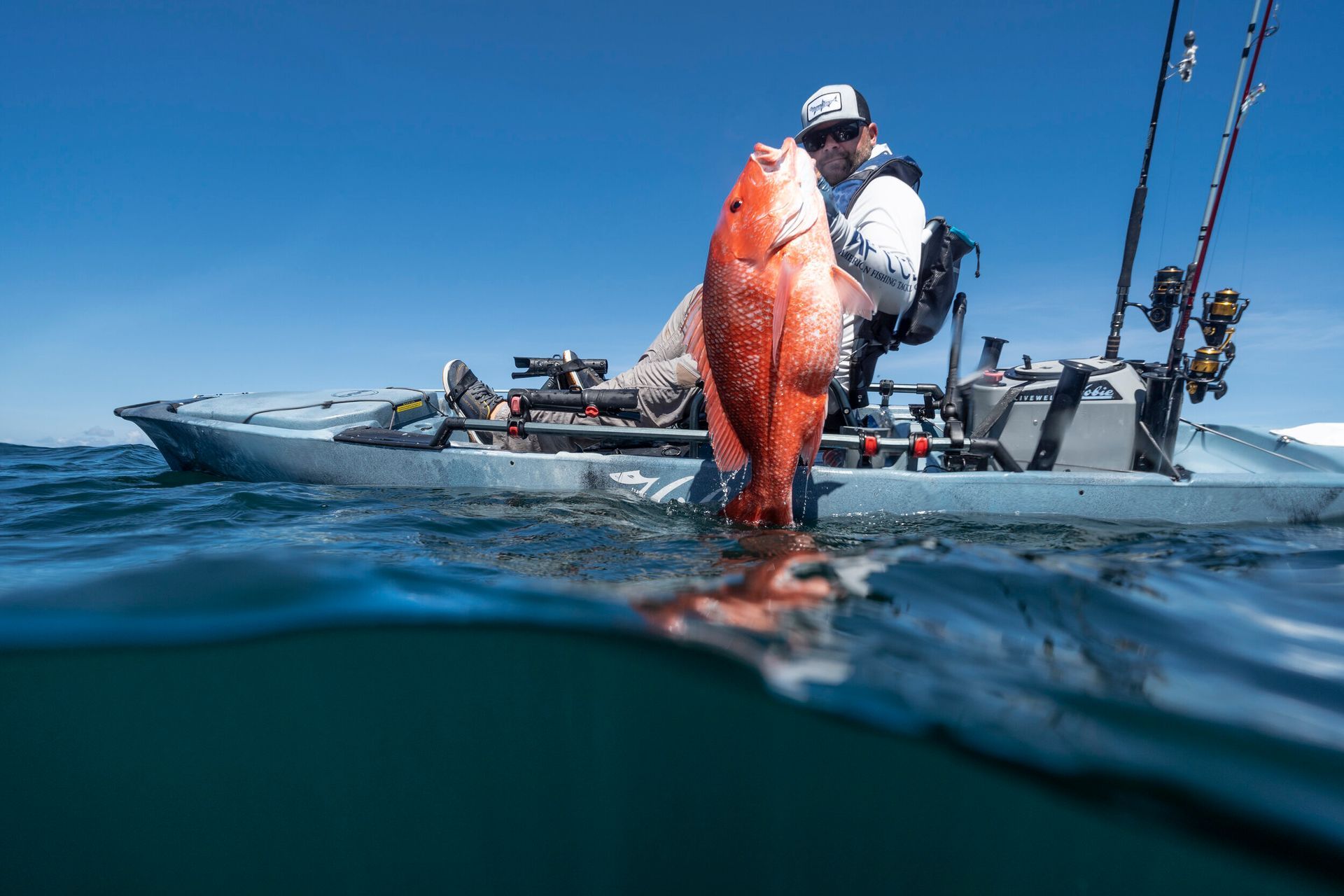 A man in a kayak is holding a large red fish in the water.