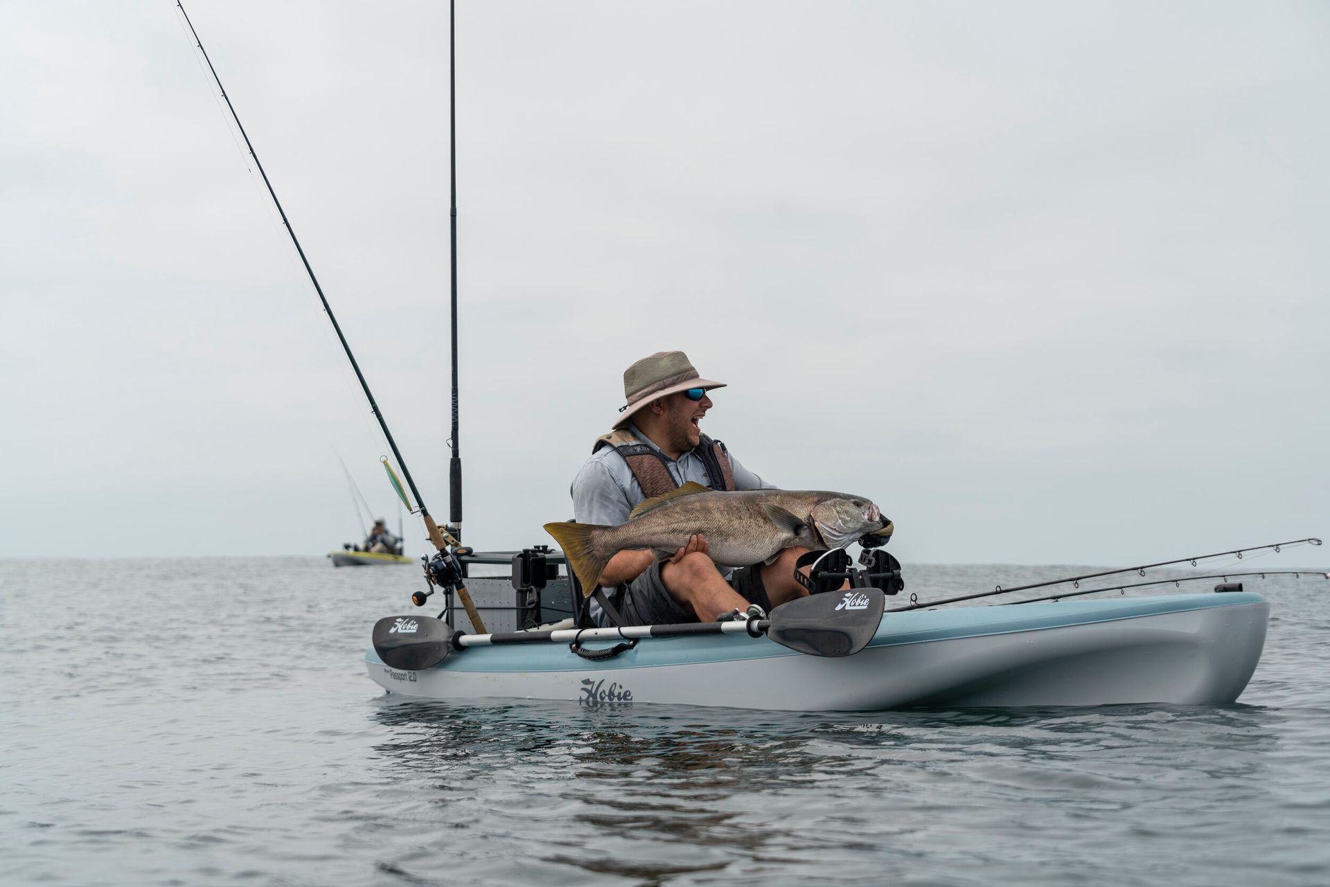 A man is sitting in a kayak holding a large fish.