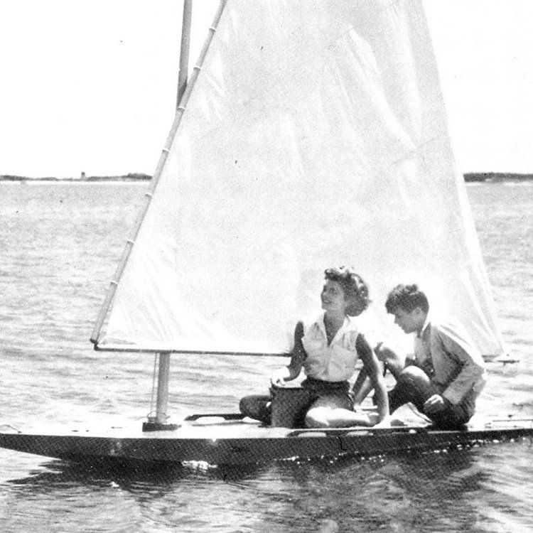 A boy and a girl are sitting on a sailboat in the water.