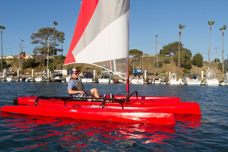 A man is sitting on a red sailboat in the water.