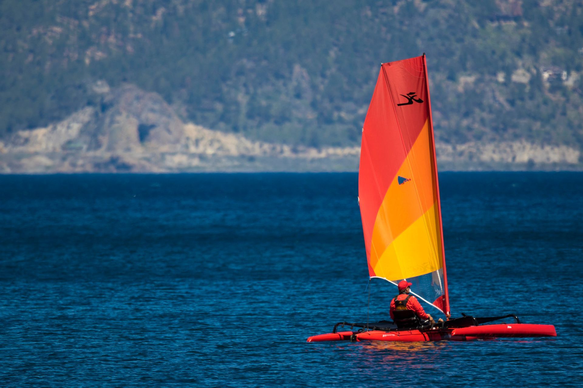A person is sailing a red and yellow sailboat in the ocean.