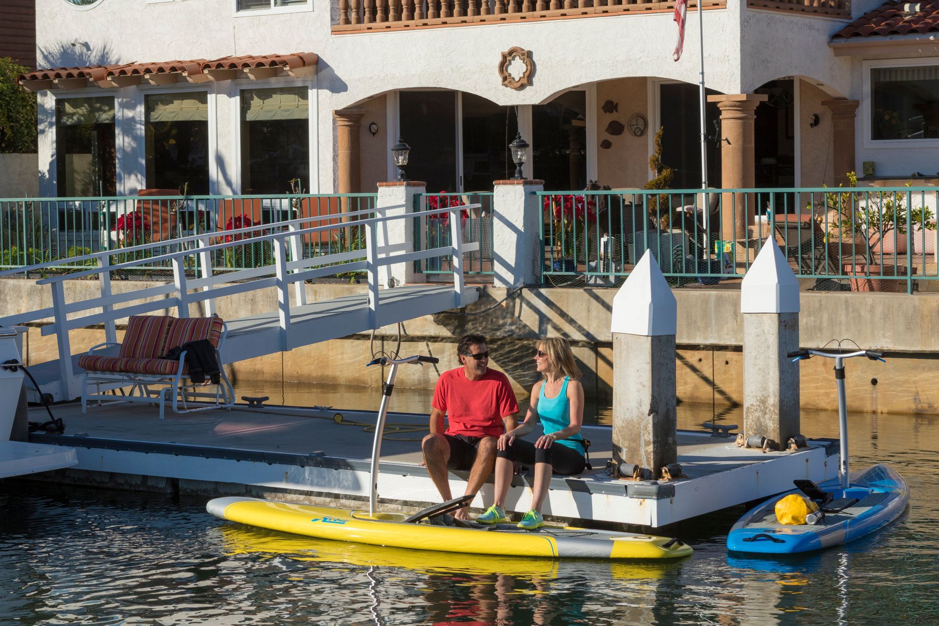 A man and a woman are sitting on a paddle board in front of a house.