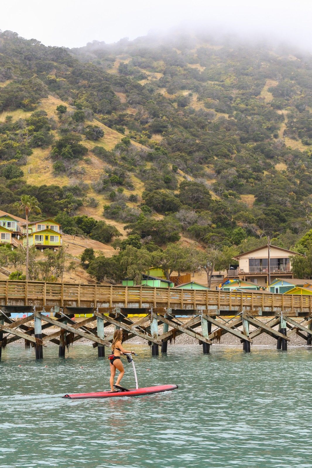 A person is riding a paddle board in the water near a dock.