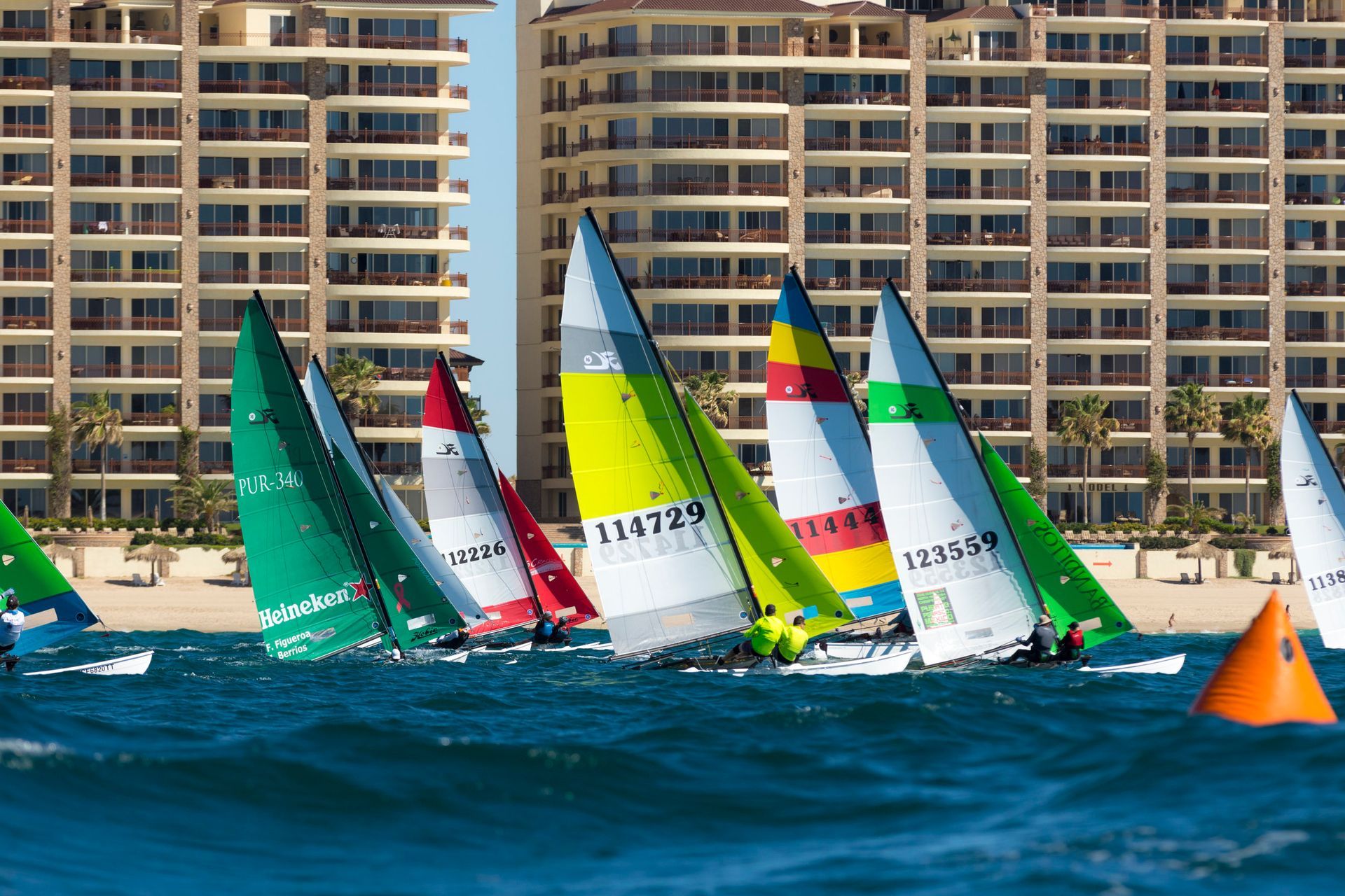 A group of sailboats are racing in the ocean with a building in the background.