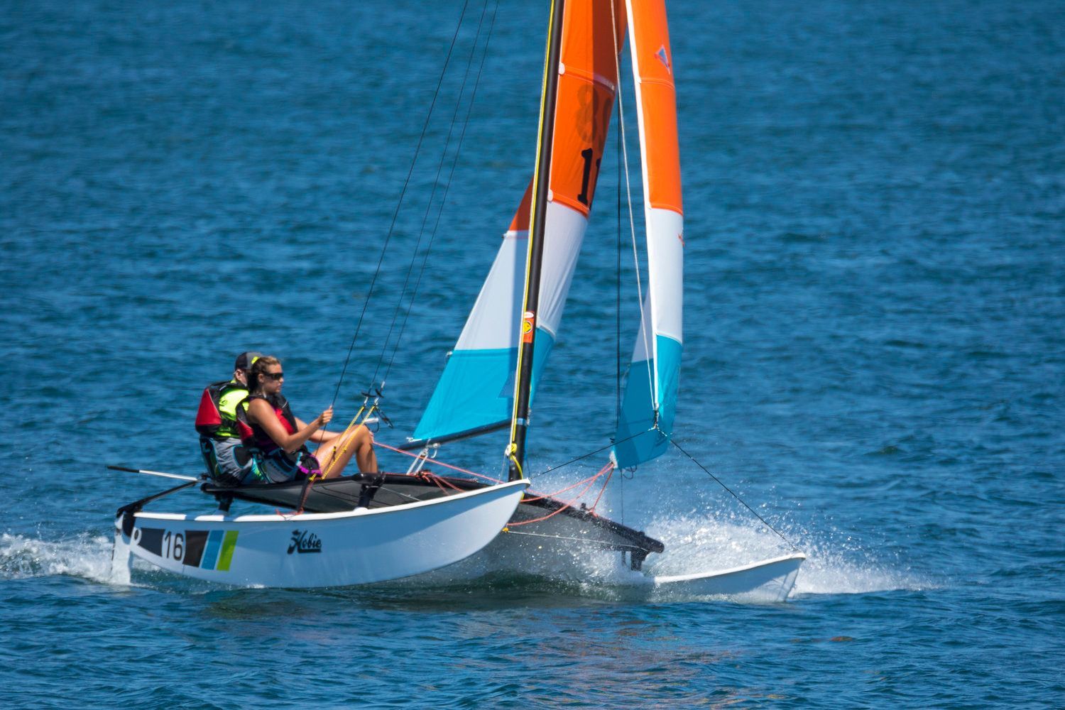 Two people are sailing a small sailboat on a lake.