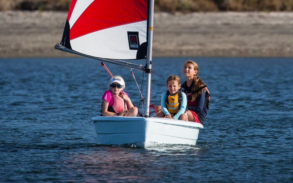 A woman and two children are sailing a small boat on a lake.