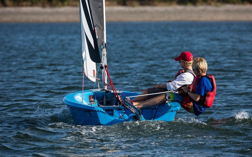 Two people are sailing a small blue boat on a lake.