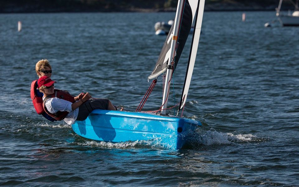 Two people are sailing a small blue boat on a lake.