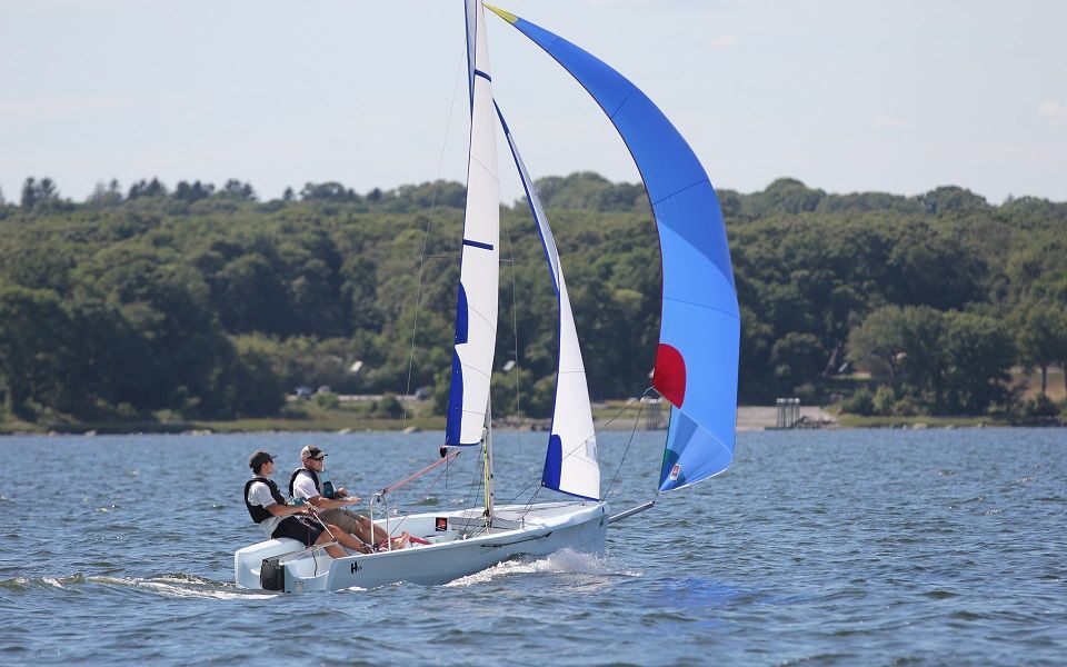 Two people are sailing a small sailboat on a lake.