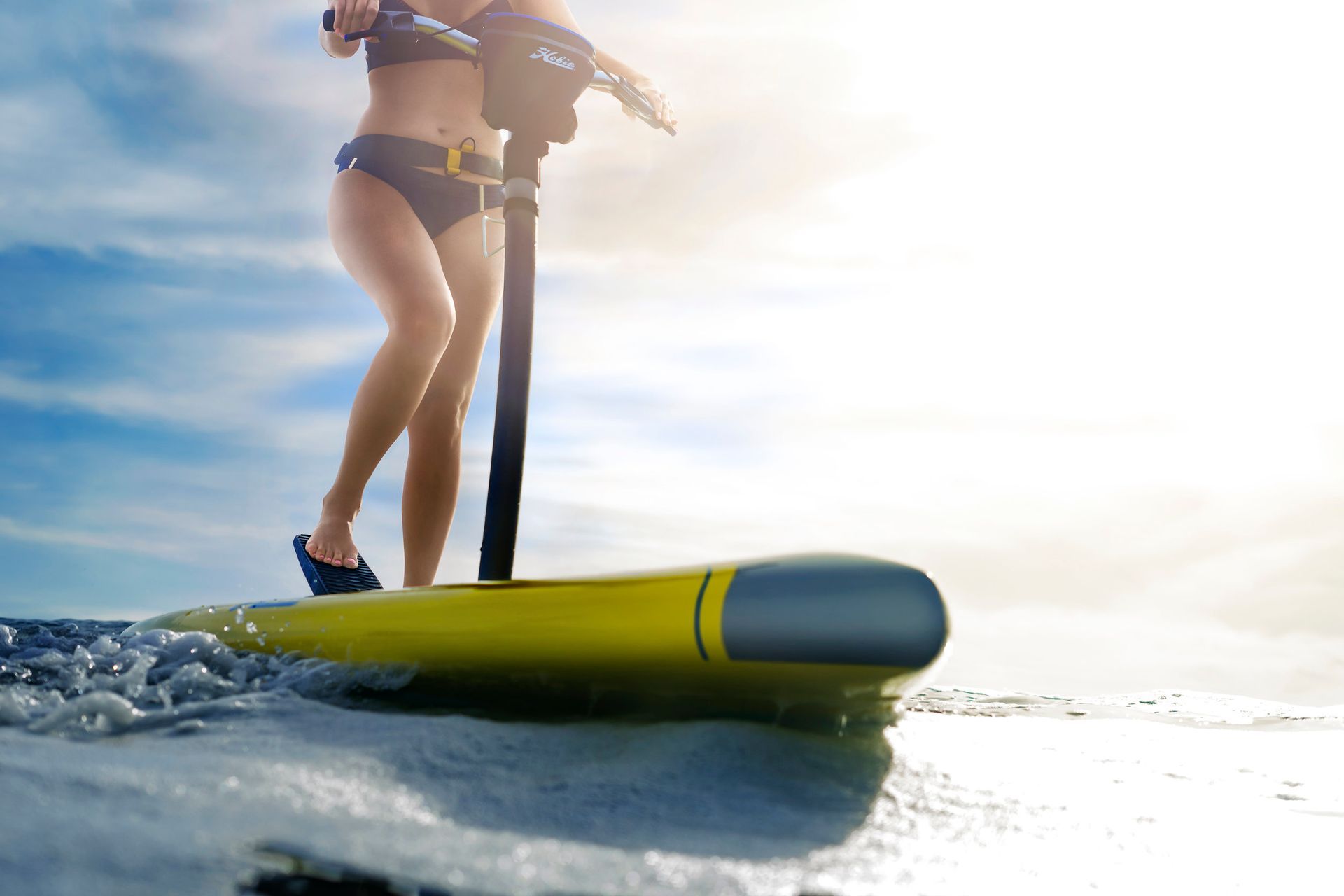 A woman in a bikini is riding a yellow surfboard in the ocean.