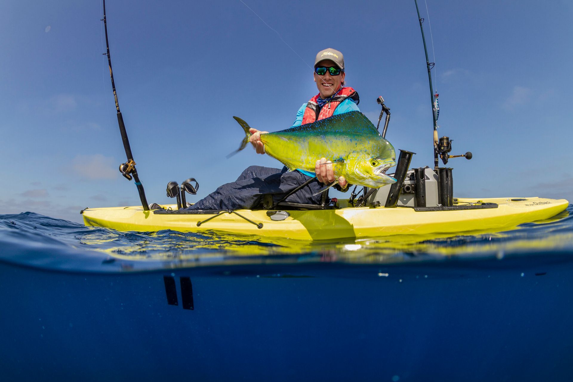 A man is sitting in a yellow kayak holding a large fish.