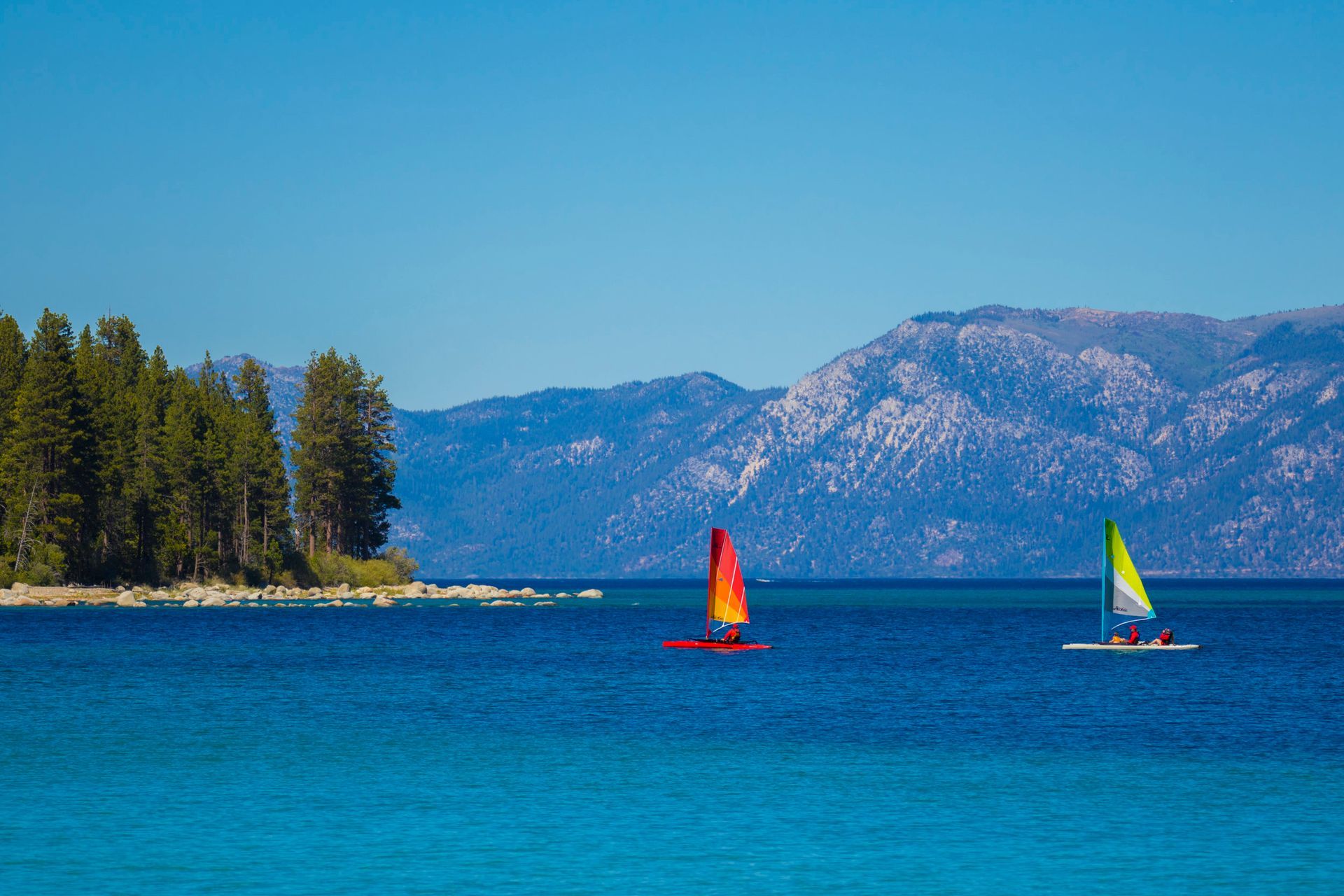 Two sailboats are floating on a lake with mountains in the background.