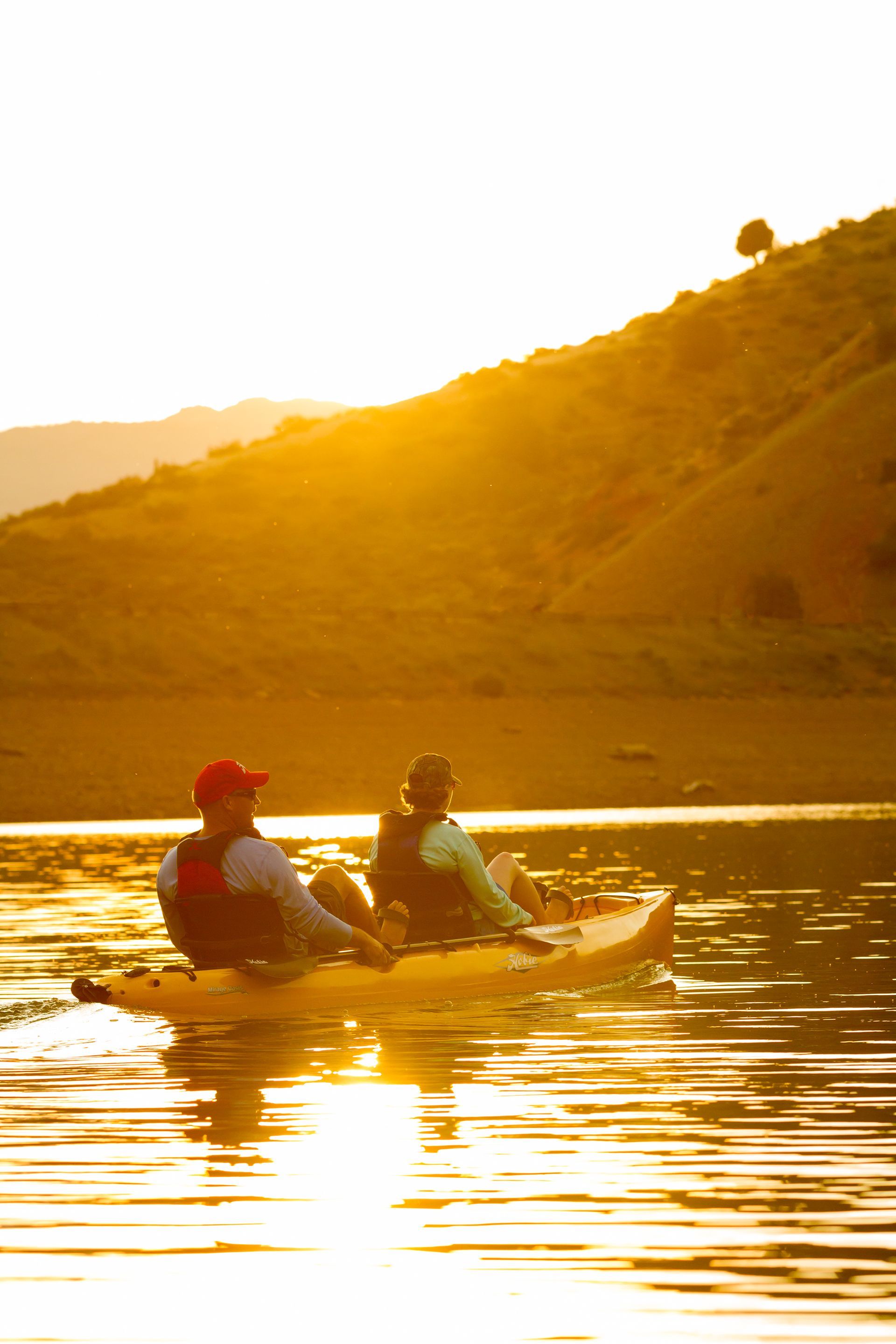 Two people are kayaking on a lake at sunset.