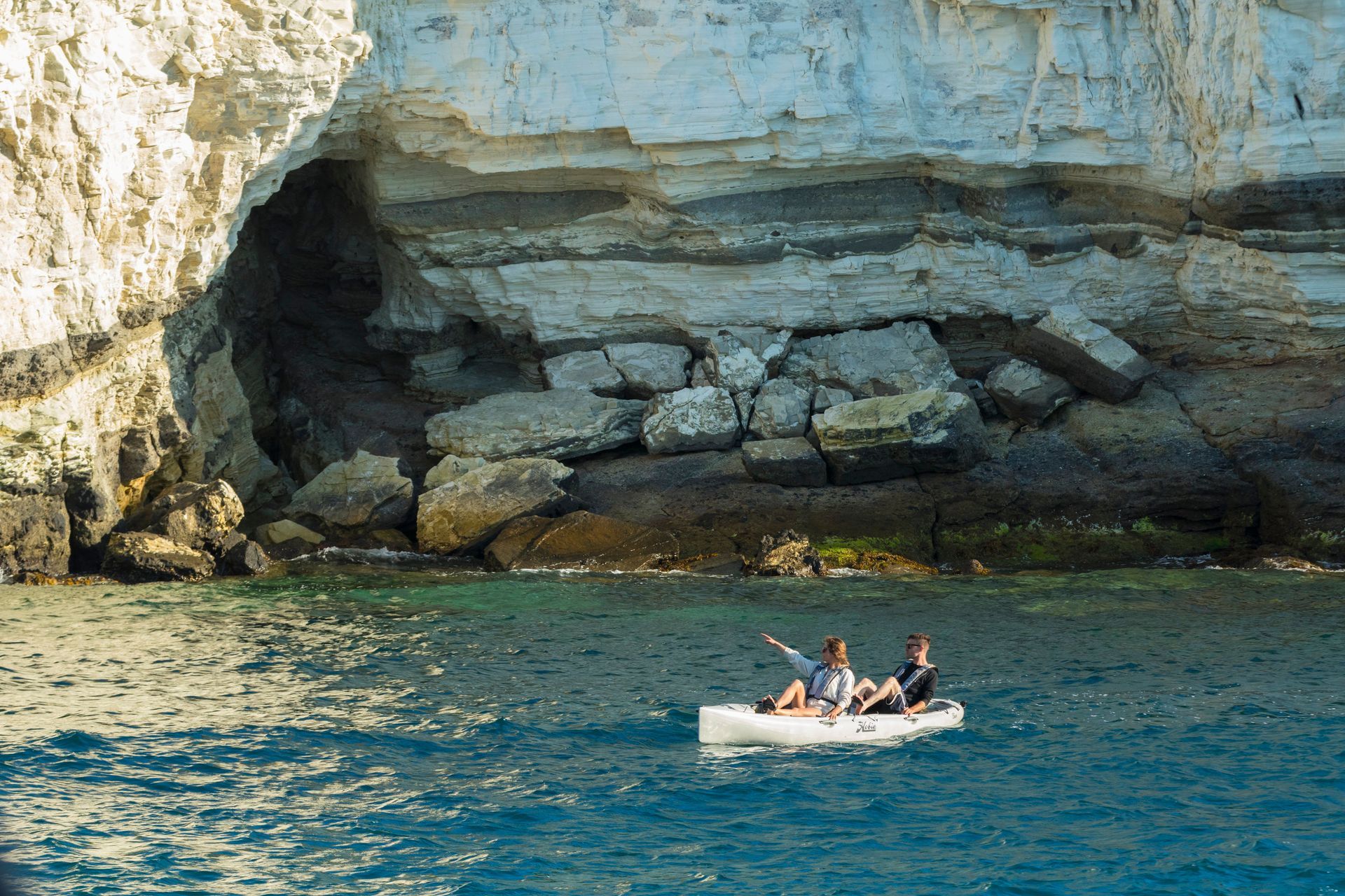 Two people are in a boat in the ocean near a cave.
