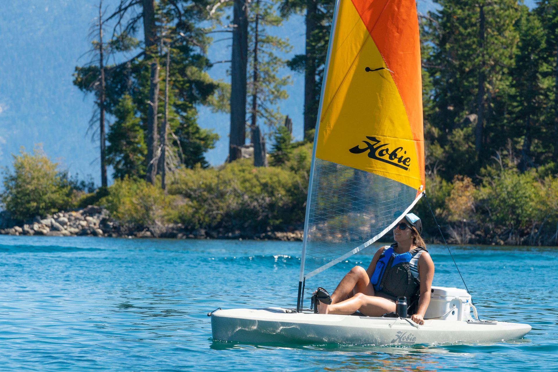 A woman is sitting on a sailboat on a lake.