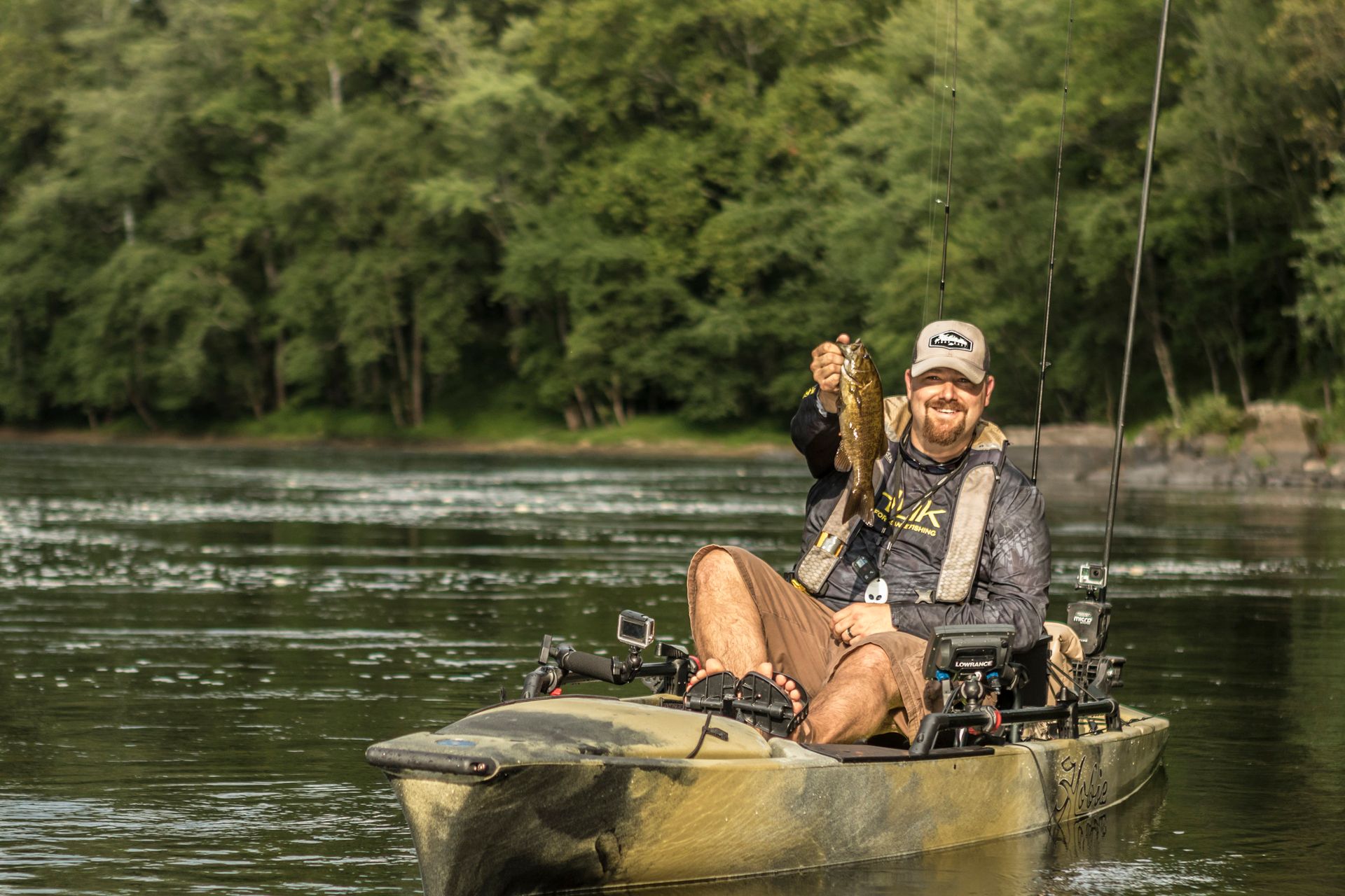 A man is sitting in a kayak on a river holding a fish.
