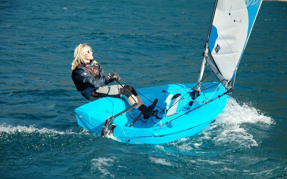 A woman is sitting on a small blue sailboat in the water.