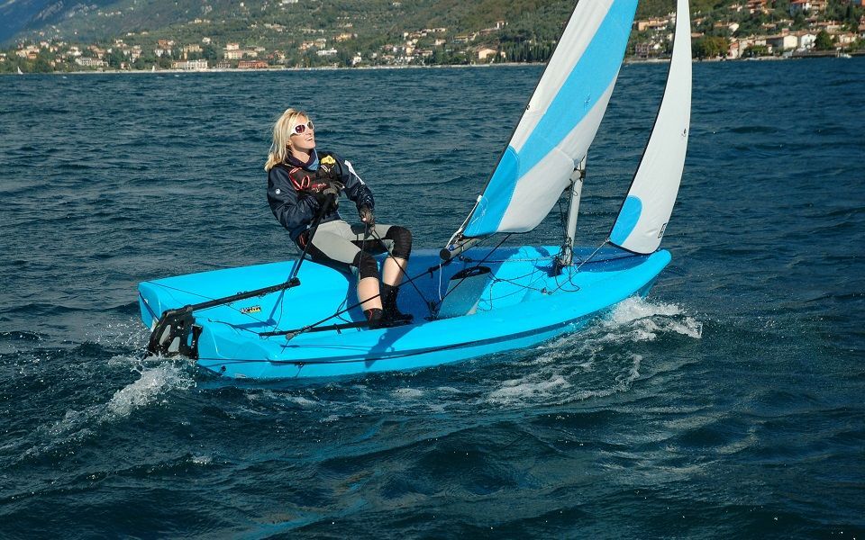 A woman is sailing a small blue sailboat on a lake.