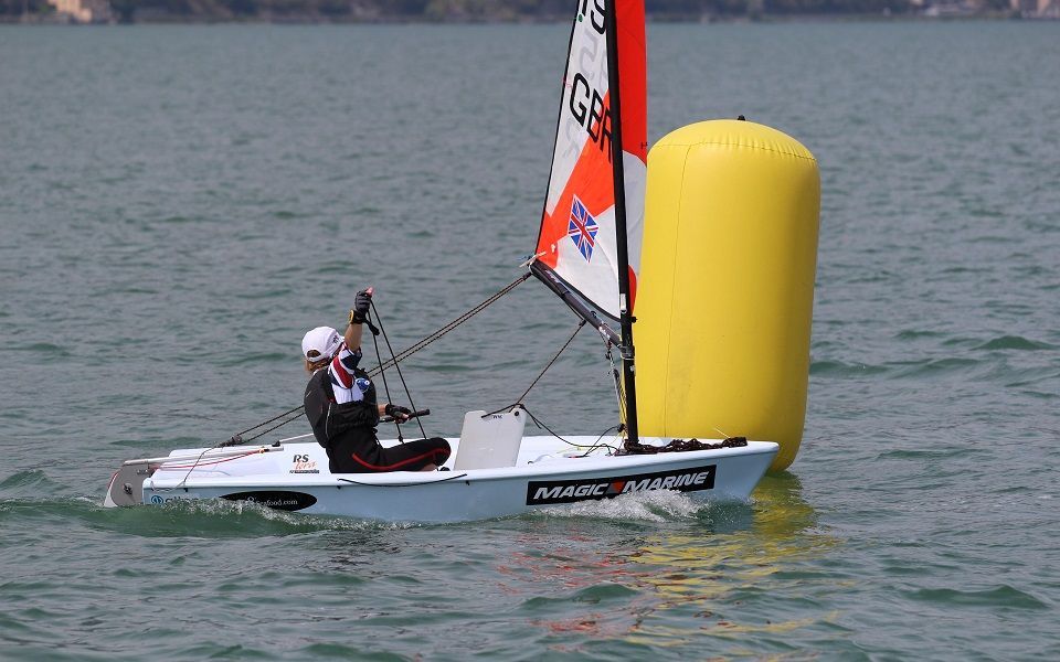 A person is sailing a small sailboat in the water next to a yellow buoy.
